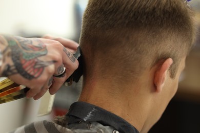 Photo of Professional barber making stylish haircut in barbershop, closeup