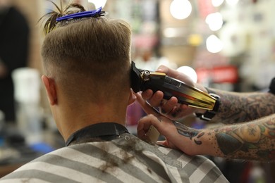 Photo of Professional barber making stylish haircut in barbershop, closeup