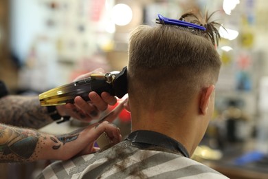 Photo of Professional barber making stylish haircut in barbershop, closeup