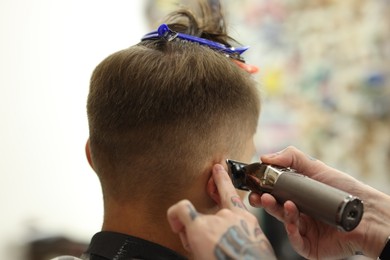 Photo of Professional barber making stylish haircut in barbershop, closeup