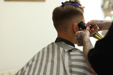 Photo of Professional barber making stylish haircut in barbershop, closeup