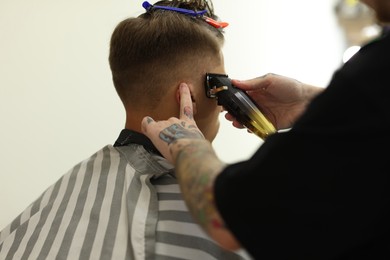 Photo of Professional barber making stylish haircut in barbershop, closeup
