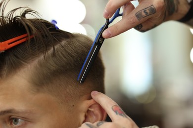 Photo of Professional barber cutting client's hair with scissors in barbershop, closeup