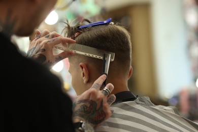Photo of Professional barber cutting client's hair with scissors in barbershop, closeup