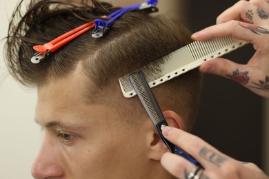 Photo of Professional barber cutting client's hair with scissors in barbershop, closeup