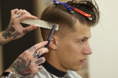 Photo of Professional barber cutting client's hair with scissors in barbershop, closeup