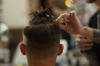 Photo of Professional barber making stylish haircut in barbershop, closeup
