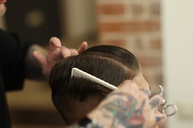 Photo of Professional barber making stylish haircut in barbershop, closeup