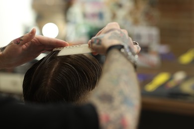 Photo of Professional barber making stylish haircut in barbershop, closeup