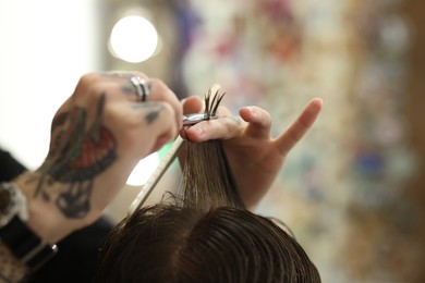 Photo of Professional barber cutting client's hair with scissors in barbershop, closeup