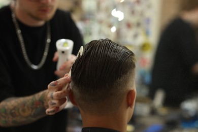 Photo of Professional barber cutting client's hair with scissors in barbershop, closeup