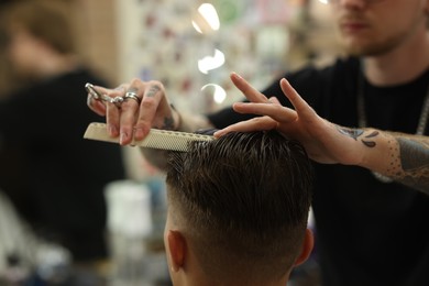 Photo of Professional barber making stylish haircut in barbershop, closeup