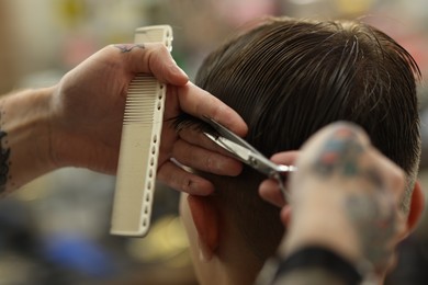 Photo of Professional barber cutting client's hair with scissors in barbershop, closeup