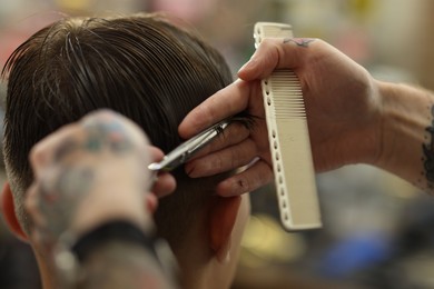 Photo of Professional barber cutting client's hair with scissors in barbershop, closeup