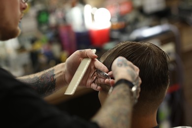 Photo of Professional barber cutting client's hair with scissors in barbershop, closeup