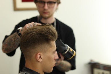 Photo of Professional barber blow drying client's hair in barbershop, selective focus. Space for text