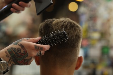 Photo of Professional barber blow drying client's hair in barbershop, closeup