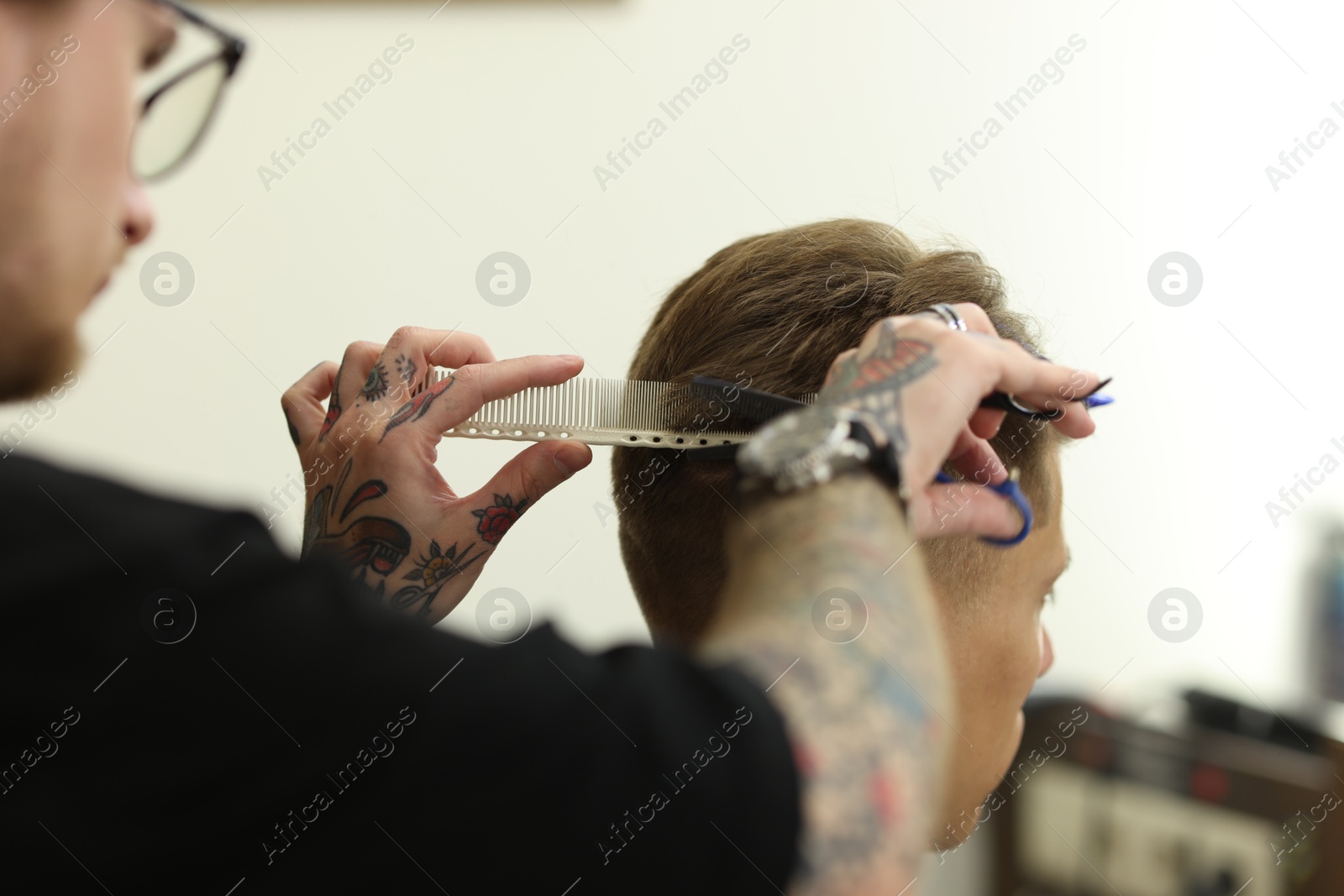 Professional barber cutting client's hair with scissors in barbershop, closeup Photo of Professional barber cutting client's hair with scissors in barbershop, closeup