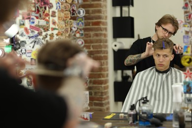 Photo of Professional barber cutting client's hair with scissors in barbershop, selective focus