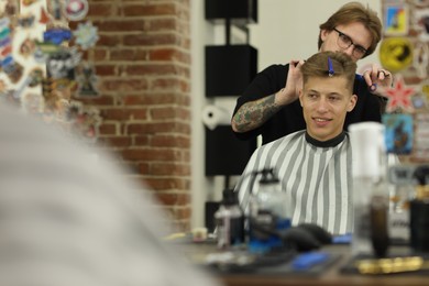 Photo of Professional barber cutting client's hair with scissors in barbershop, selective focus