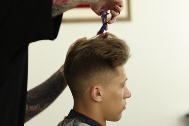 Photo of Professional barber cutting client's hair with scissors in barbershop, closeup