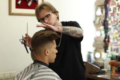 Photo of Professional barber making stylish haircut in barbershop, selective focus
