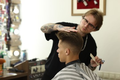 Photo of Professional barber making stylish haircut in barbershop, selective focus