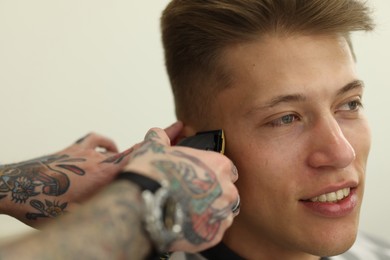 Photo of Professional barber making stylish haircut in barbershop, closeup