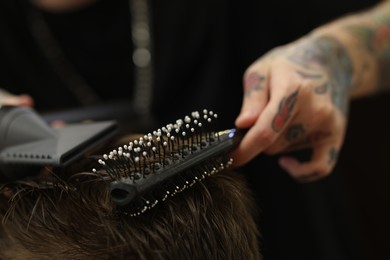 Photo of Professional barber blow drying client's hair in barbershop, closeup