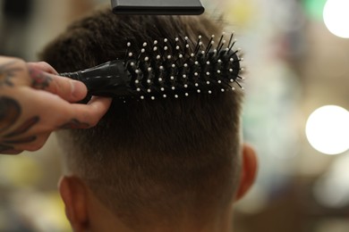 Photo of Professional barber blow drying client's hair in barbershop, closeup