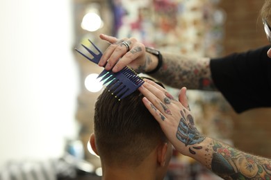 Photo of Professional barber making stylish haircut in barbershop, closeup