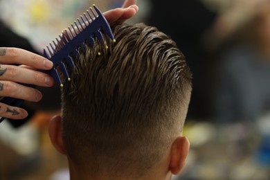 Photo of Professional barber making stylish haircut in barbershop, closeup