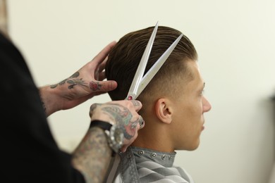 Photo of Professional barber cutting client's hair with scissors in barbershop, closeup