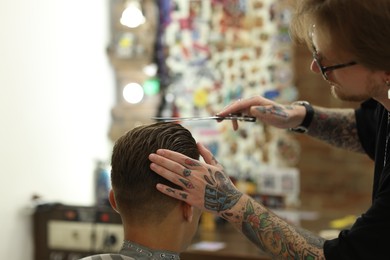 Photo of Professional barber cutting client's hair with scissors in barbershop