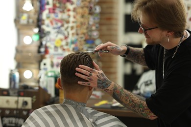 Photo of Professional barber cutting client's hair with scissors in barbershop