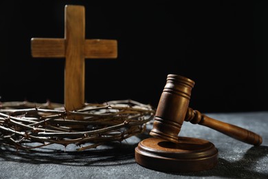 Photo of Crown of thorns, judge's gavel and wooden cross on dark textured background, closeup