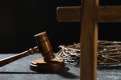 Photo of Crown of thorns, judge's gavel and wooden cross on dark textured background, closeup