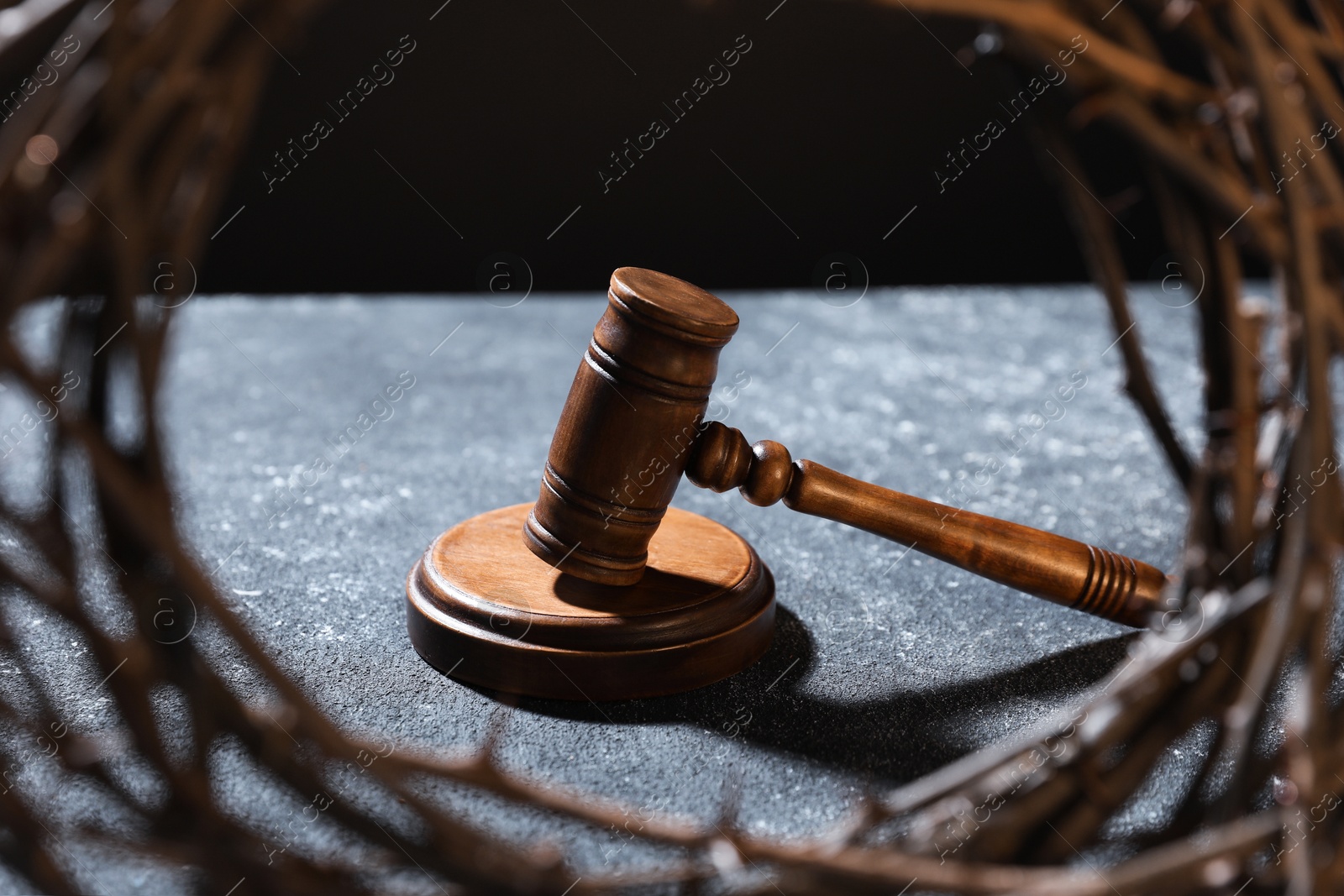View of judge's gavel through crown of thorns on dark textured table Photo of View of judge's gavel through crown of thorns on dark textured table