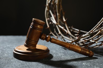 Photo of Crown of thorns and judge's gavel on dark textured background, closeup