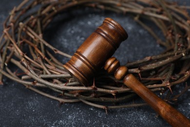 Photo of Crown of thorns and judge's gavel on dark textured background, closeup