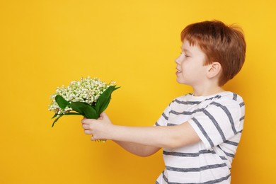 Photo of Boy with bouquet of beautiful lily-of-the-valley flowers on yellow background