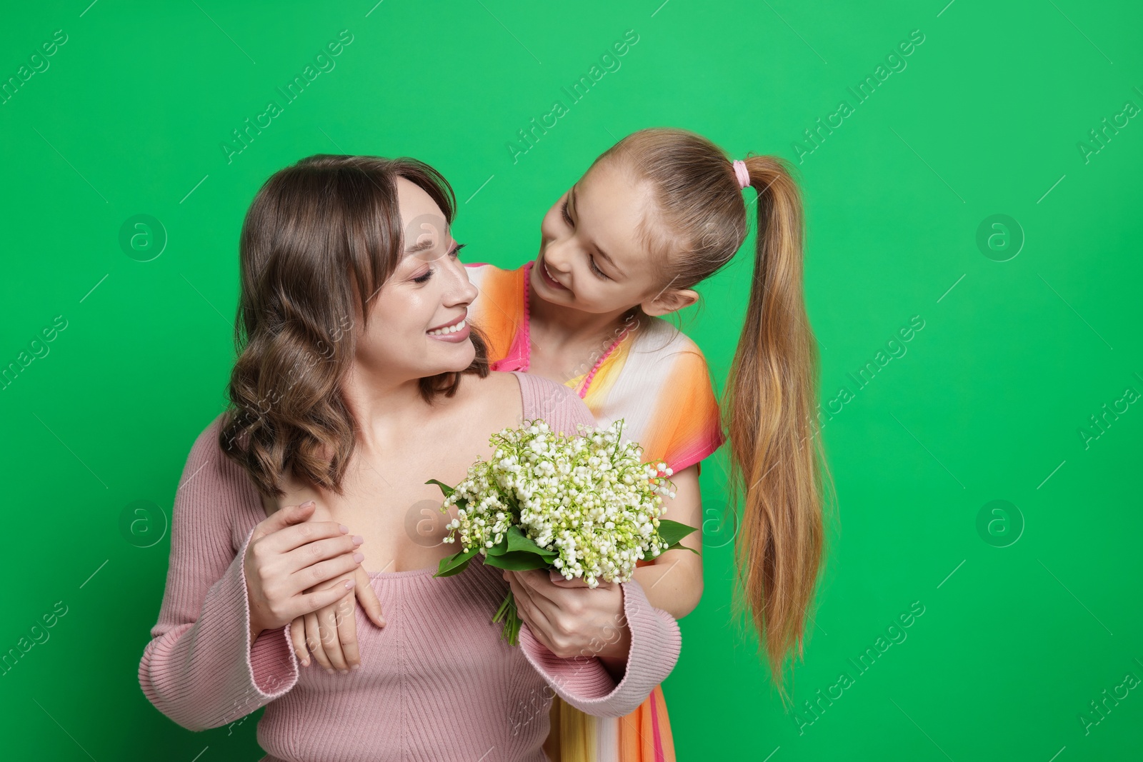 Girl giving her mother beautiful bouquet of lily-of-the-valley flowers on green background Photo of Girl giving her mother beautiful bouquet of lily-of-the-valley flowers on green background