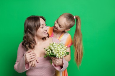 Photo of Girl giving her mother beautiful bouquet of lily-of-the-valley flowers on green background