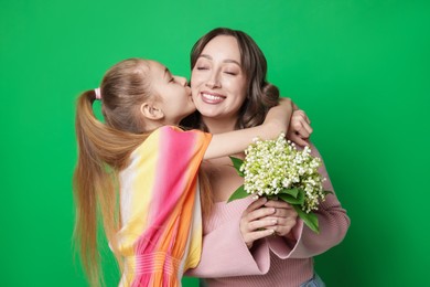 Photo of Girl kissing her mother and giving beautiful bouquet of lily-of-the-valley flowers on green background