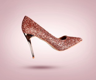 Image of Stylish sparkly high heeled shoe in air on dusty pink gradient background