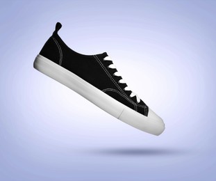 Image of Stylish black sneaker in air on light blue gradient background