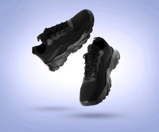 Image of Stylish black sneakers in air on light blue gradient background