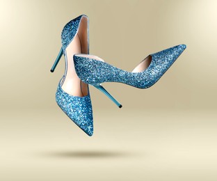 Image of Stylish sparkly high heel shoes in air on beige gradient background