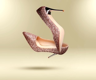 Image of Stylish sparkly high heel shoes in air on beige gradient background