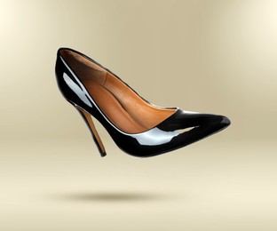 Image of Stylish black high heeled shoe in air on beige gradient background